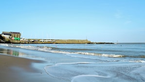 A coastal scene with a sandy beach, a building with a green roof, and boats docked near the shore. - 5 bedroom accommodation in New Quay (New Quay)