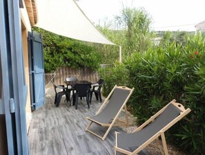 An outdoor patio with a wooden table and chairs, two lounge chairs, and a large white canopy.