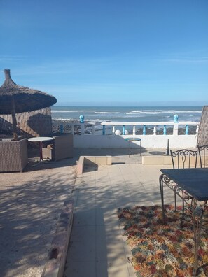 A patio area with a view of the ocean, outdoor furniture, and a thatched-roof structure. - Direct beachfront bungalow (Tamaris)