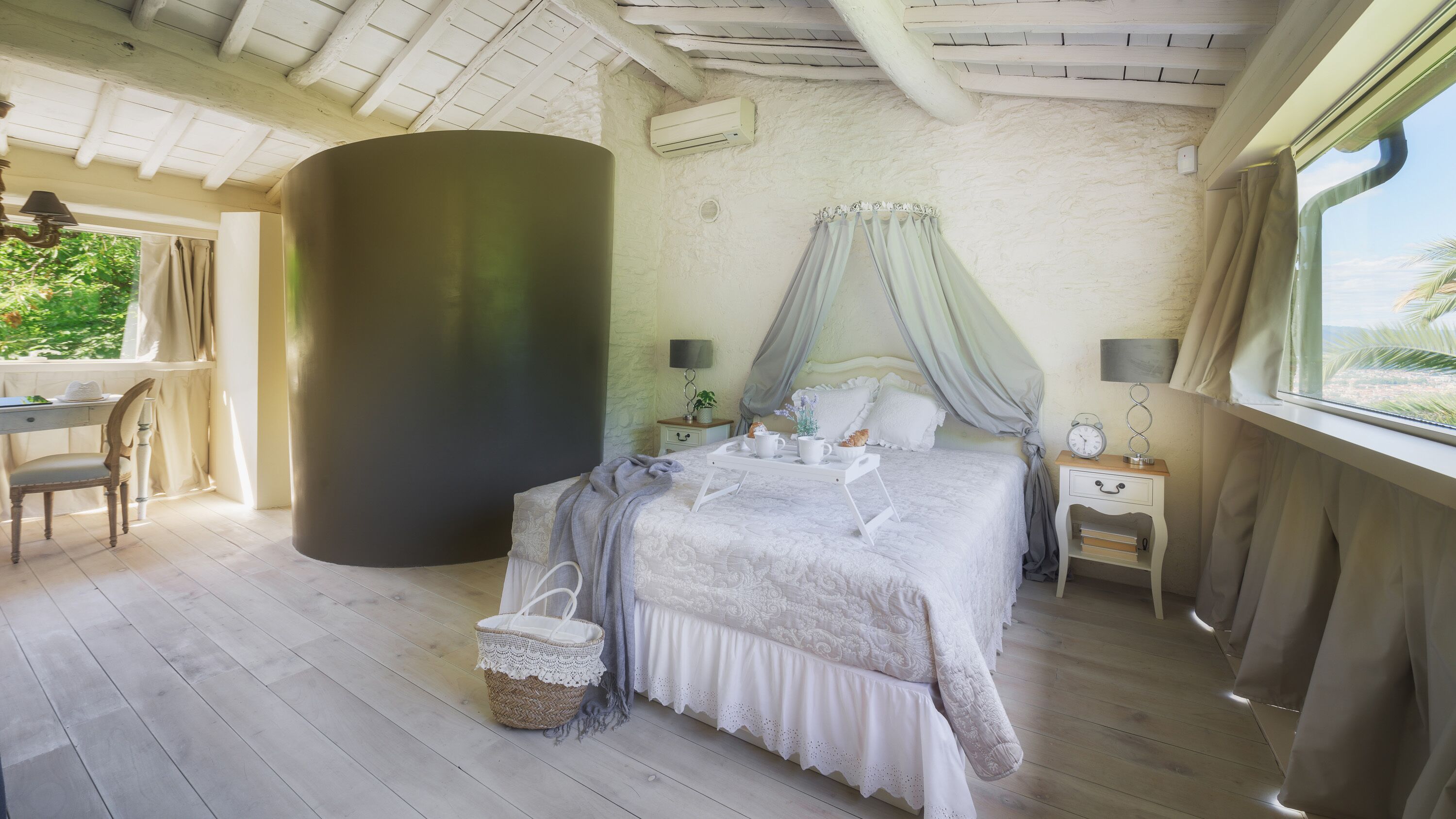 A bedroom with a large bed, a bedside table with a lamp, a nightstand, and a window with curtains.