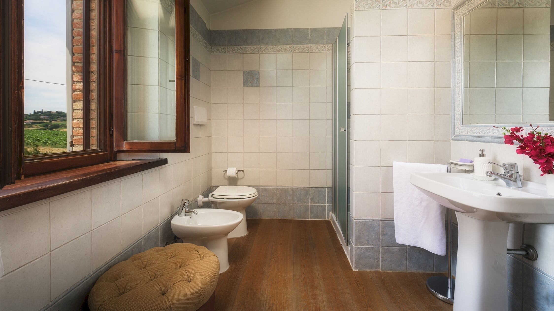 Un baño con ventana, dos inodoros, un lavamanos y suelo de madera.