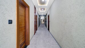 A long, narrow hallway with wooden doors on one side and a plain wall on the other. - Itsy Hotels Anjali Mahal 500, Mtrs From Mathura Railway Station (Mathura)