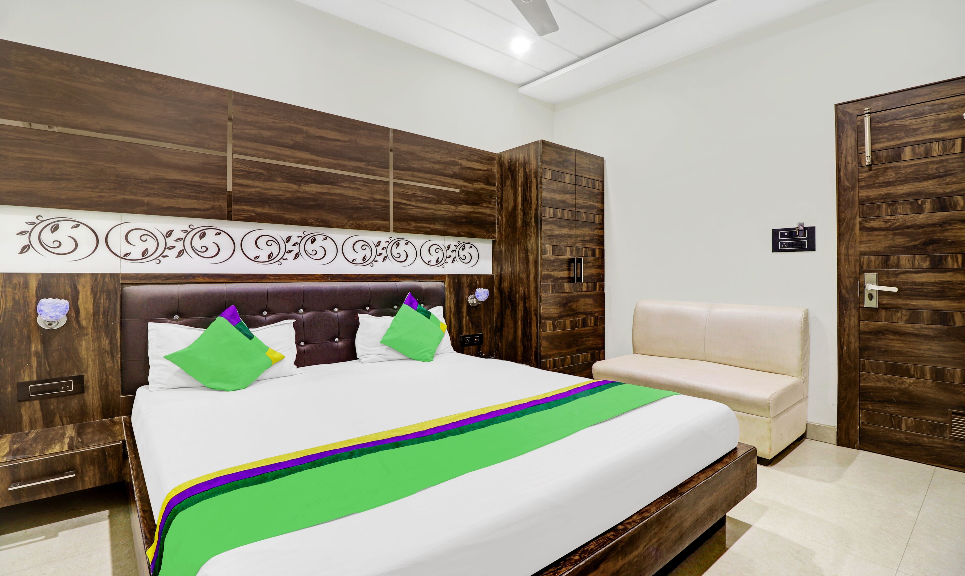 A bedroom with a large bed, a sofa, wooden paneling, and a decorative wall panel.