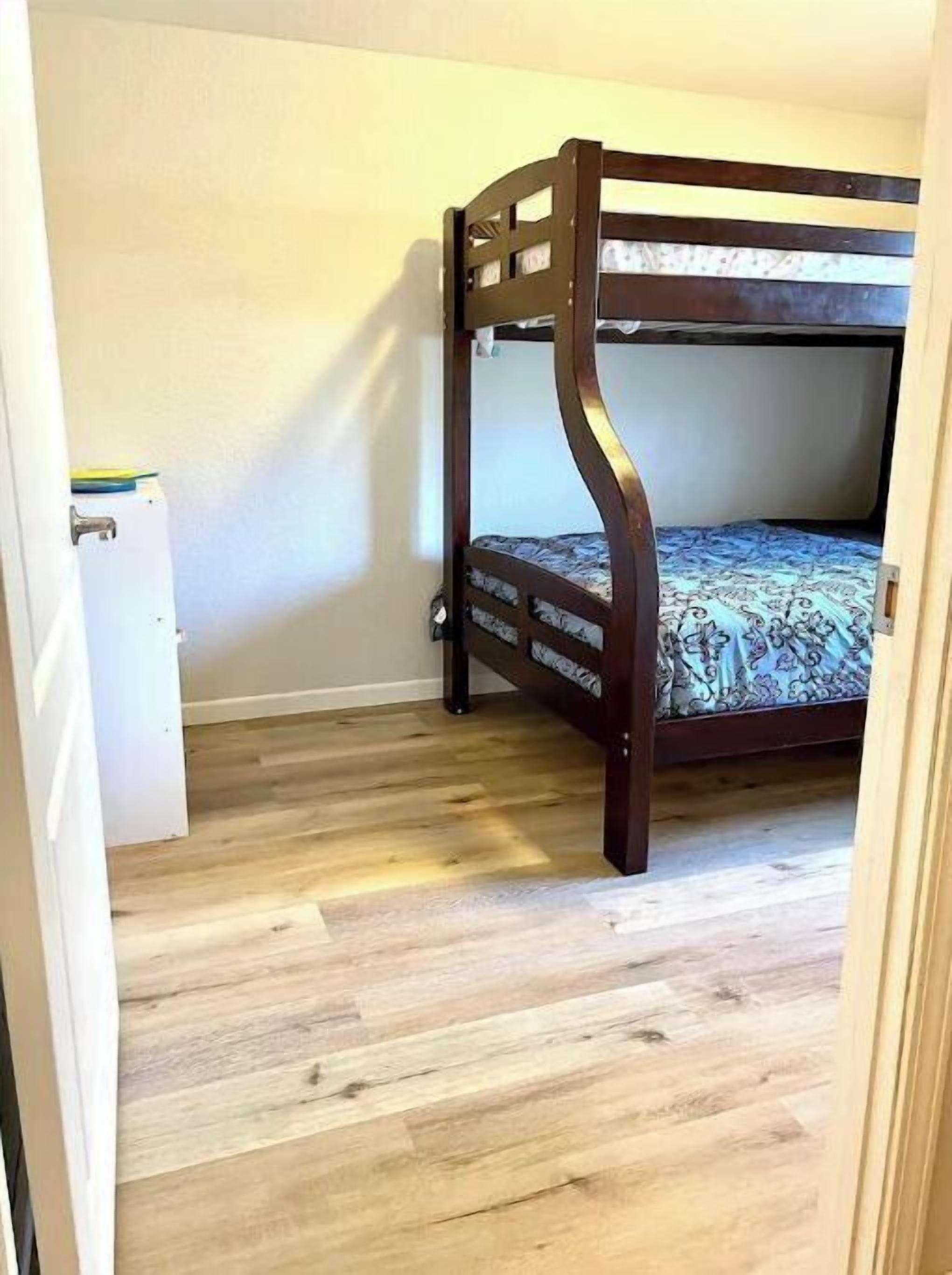 A bunk bed in a room with wooden flooring and a white door.