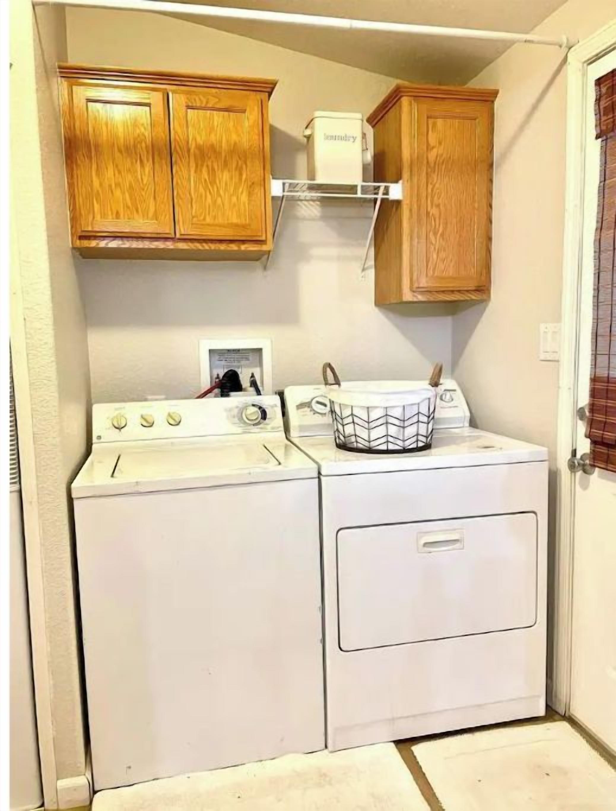 A compact laundry room with a washer and dryer, wooden cabinets, and a small window.