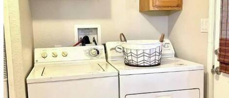 A compact laundry room with a washer and dryer, wooden cabinets, and a small window.