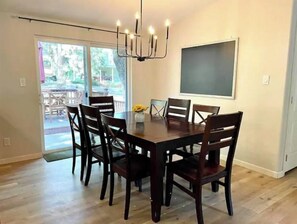 A dining room with a large wooden table and six chairs, a chandelier, and a chalkboard on the wall.