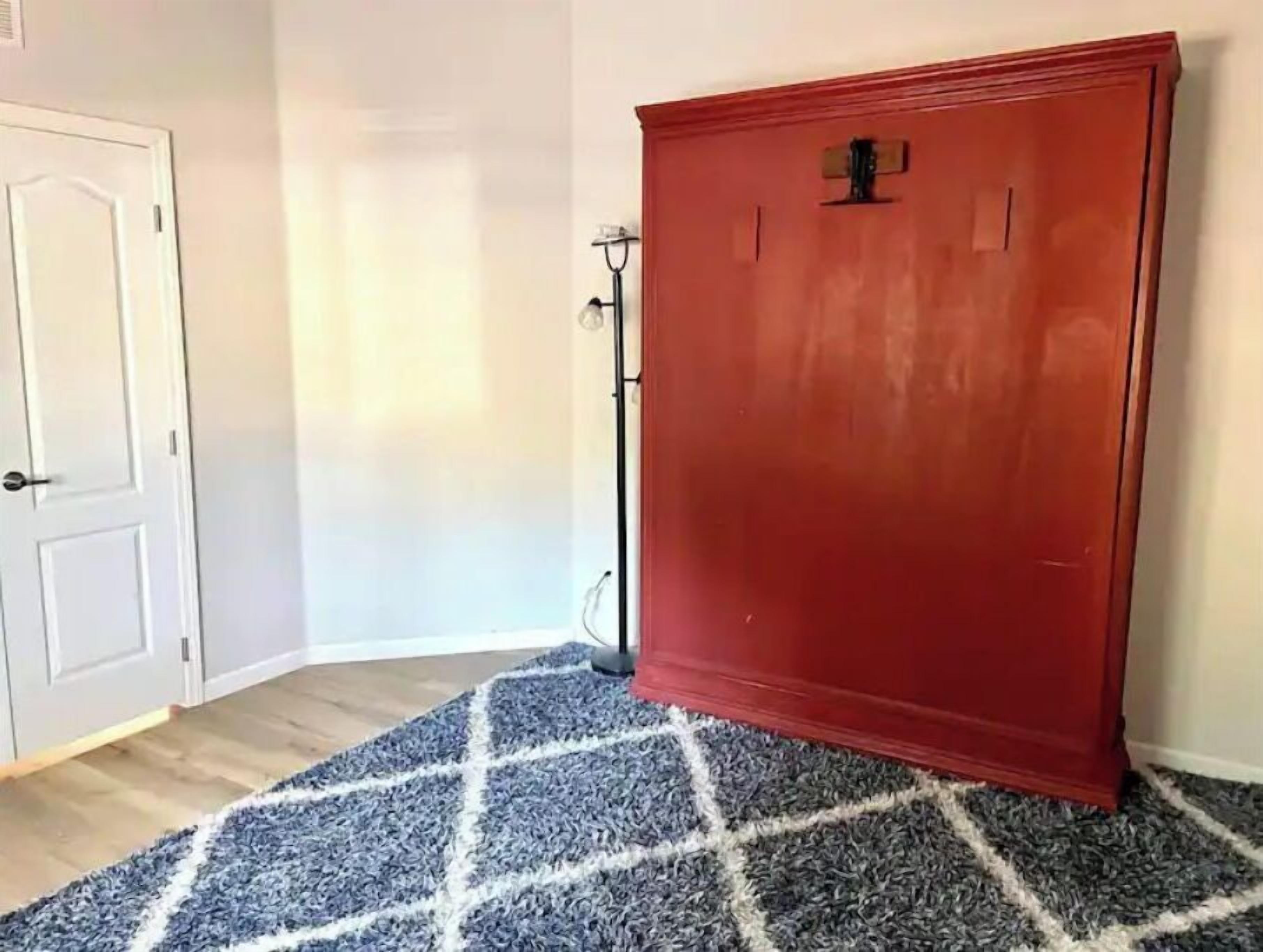 A room with a red cabinet, a white door, and a blue and white patterned rug.