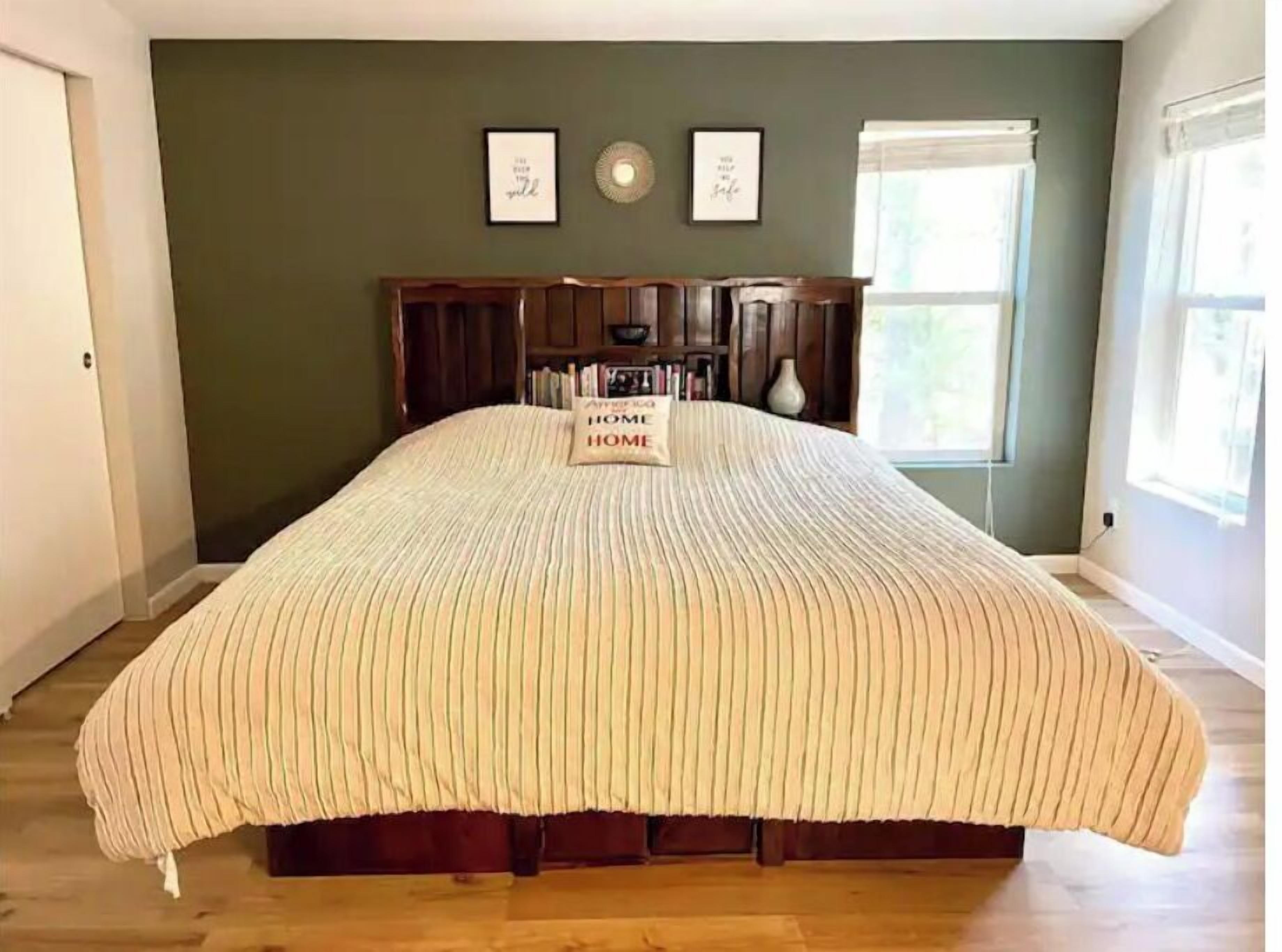 A bedroom with a large bed, a wooden headboard, a bedside table, a nightstand, a window, and a bookshelf.