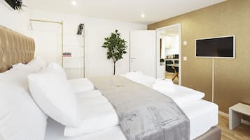 Una habitación de hotel moderna con una cama grande, una mesita de noche, un televisor, una planta y vista a la cocina a través de una puerta abierta.