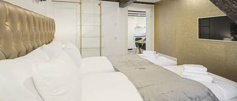 A modern hotel room with a large bed, a television mounted on the wall, and a view of the kitchen area.