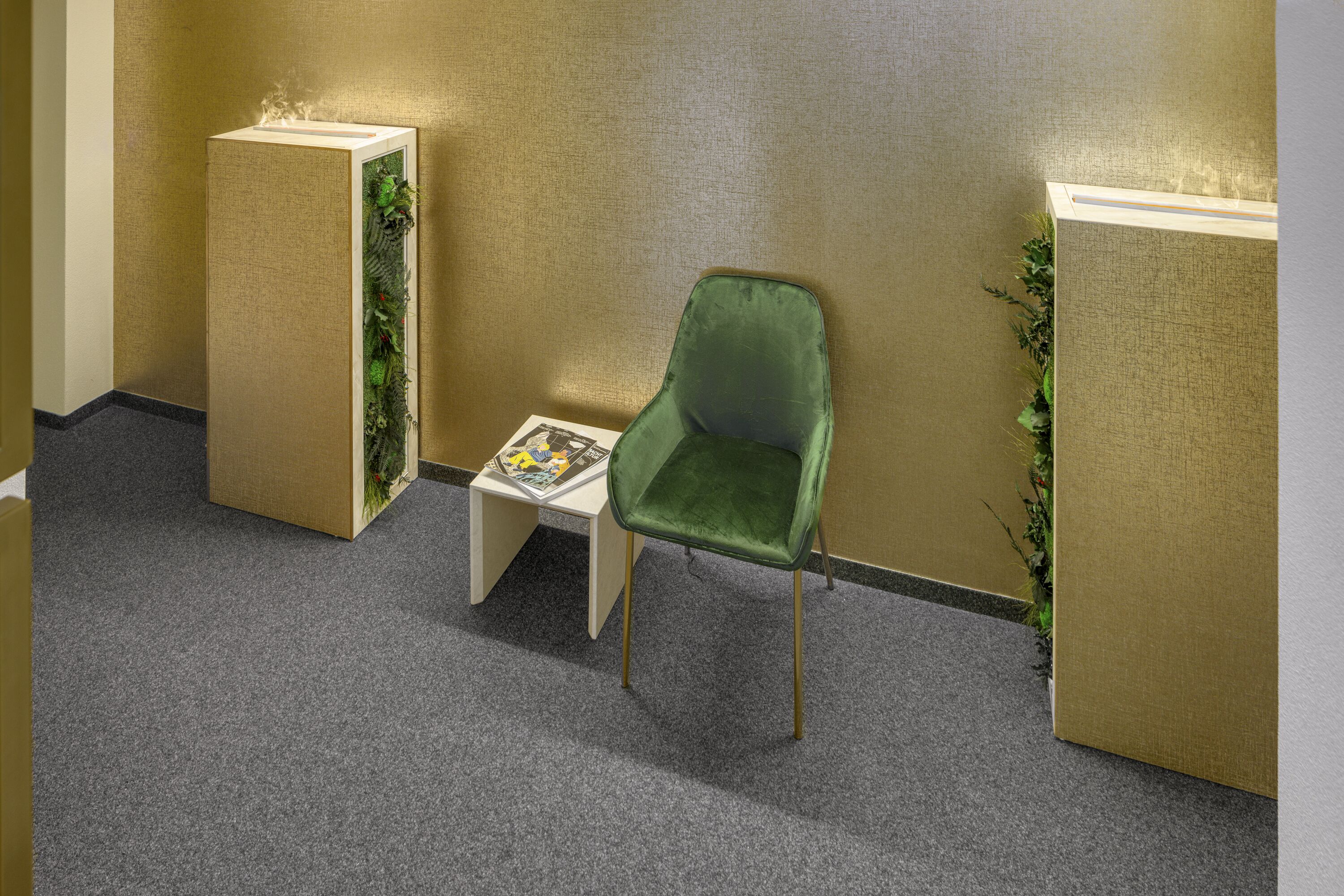 A green chair next to a small table with a magazine, against a textured wall with two vertical planters.