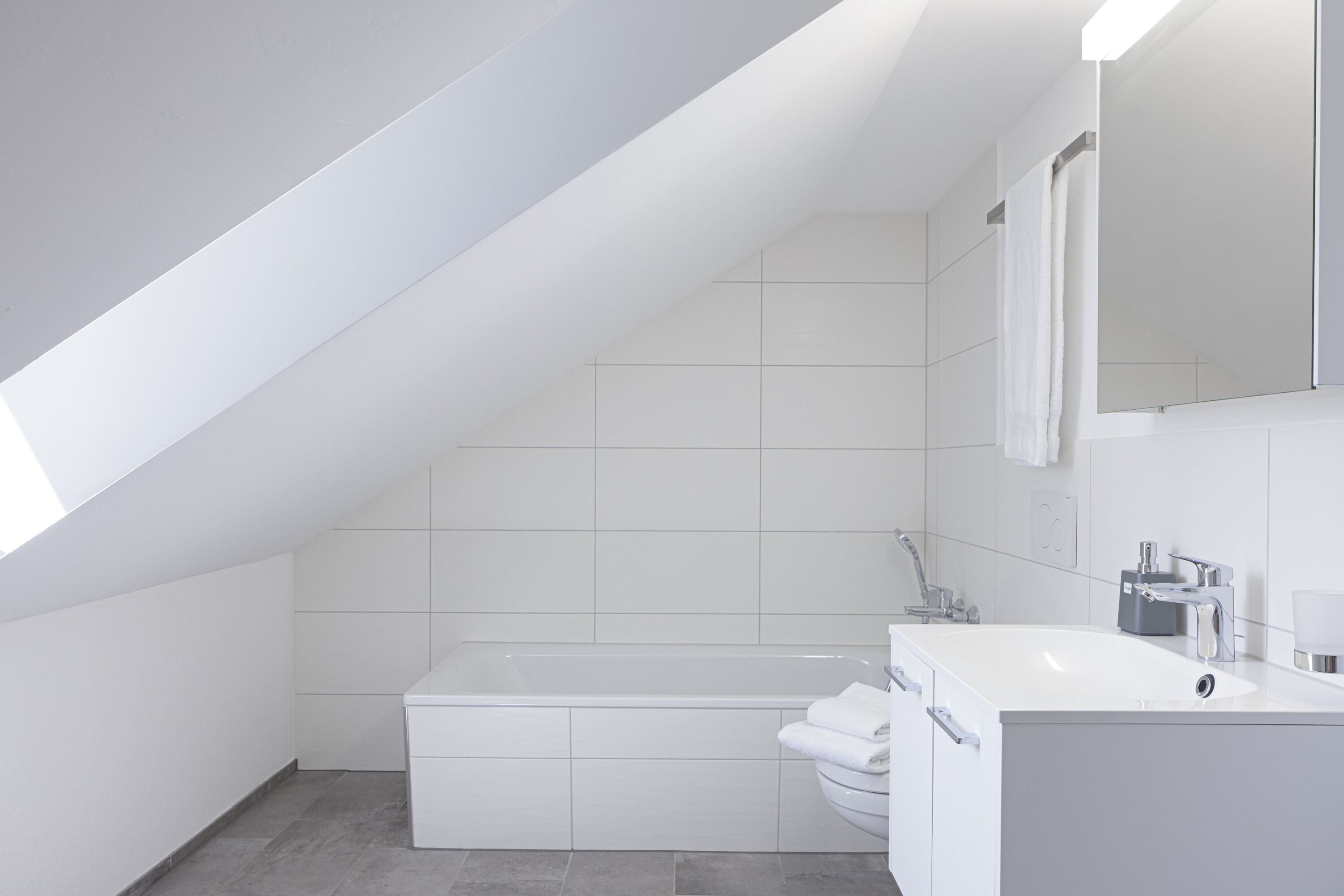 Un baño moderno con techo inclinado, bañera, inodoro y lavamanos.