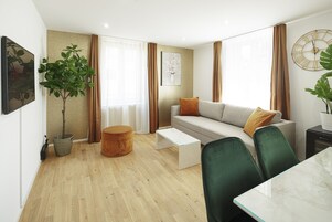 A modern living room with a sofa, coffee table, and chairs. There is a plant, a small round table, and a painting on the wall.