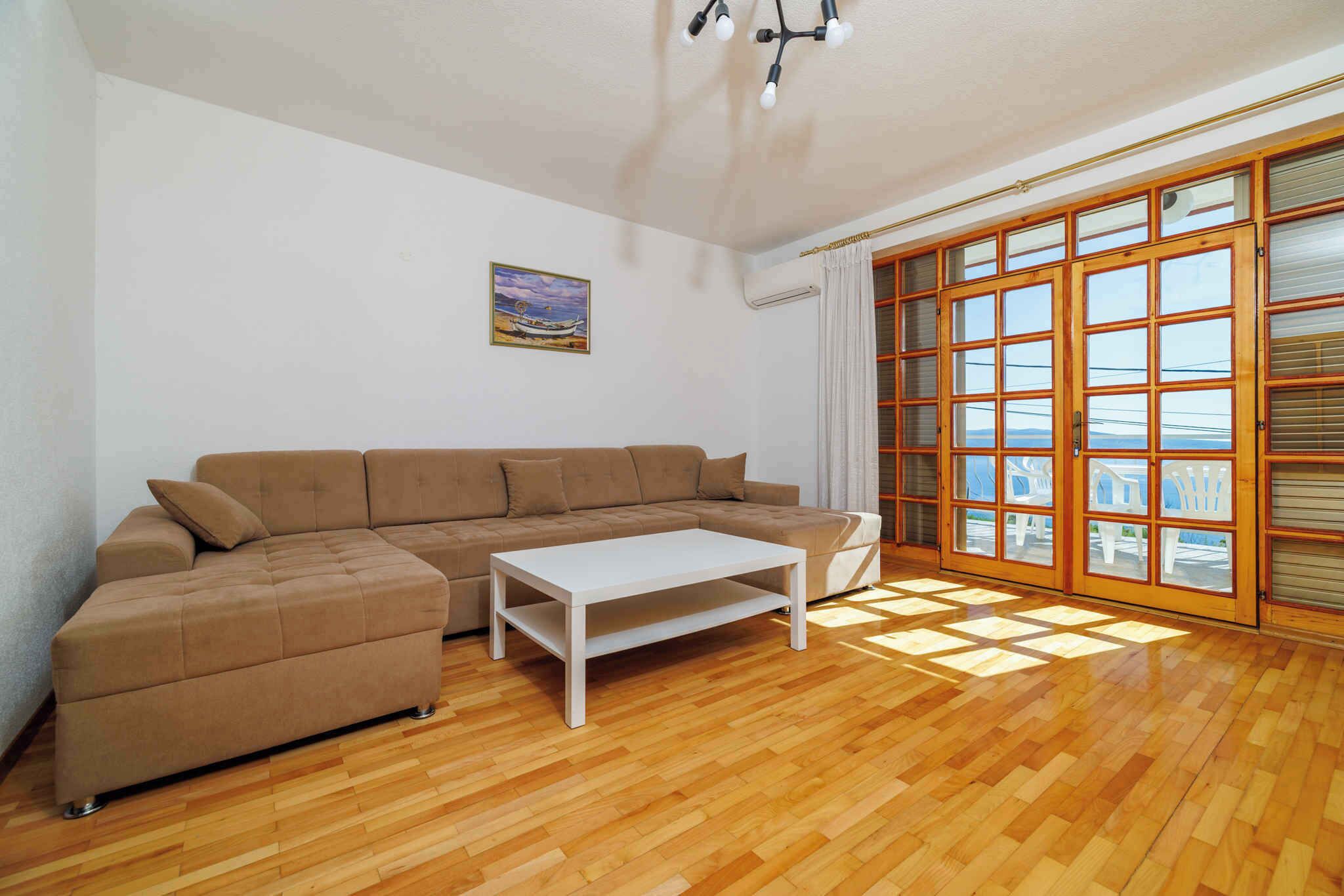 A living room with a brown sectional sofa, a white coffee table, and large windows with blinds.