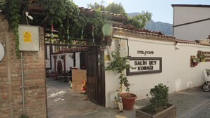 Um edifício com uma placa indicando “SALIH BEY KONAGI” e “HOTEL & CAFÉ”. Há plantas em vasos e um muro de tijolos.