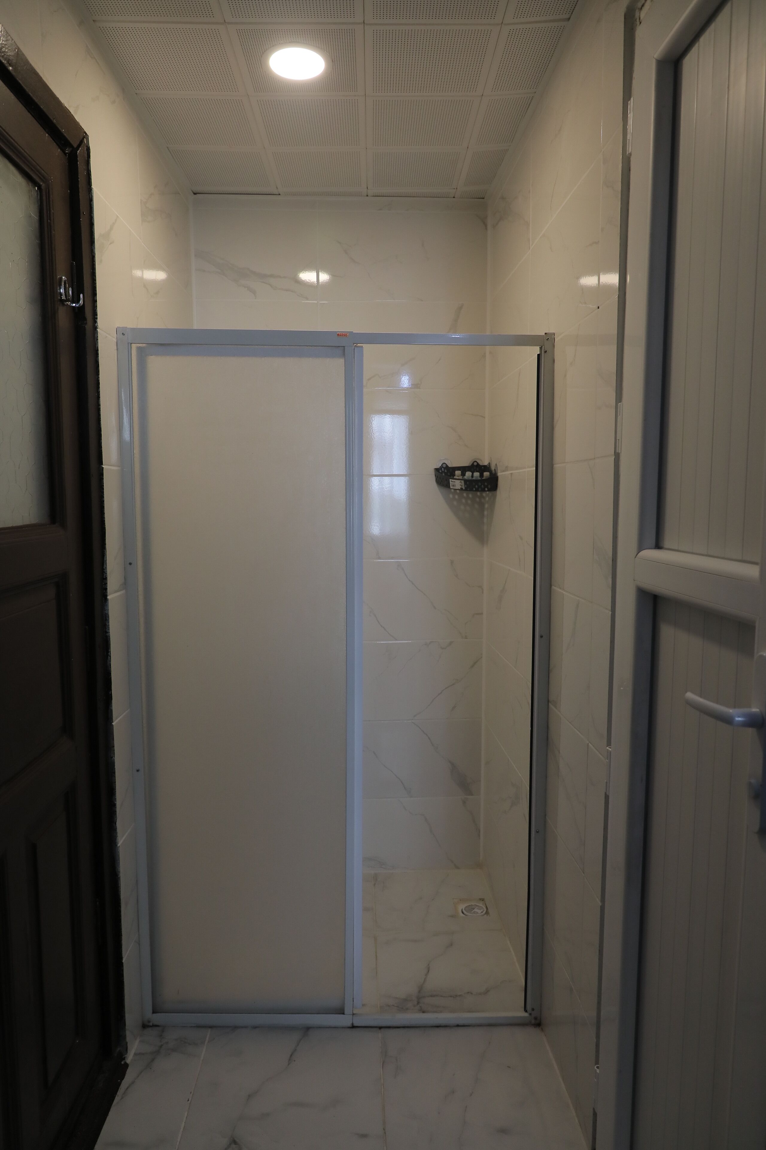 A bathroom with a glass-enclosed shower, white tiled walls, and a marble floor.