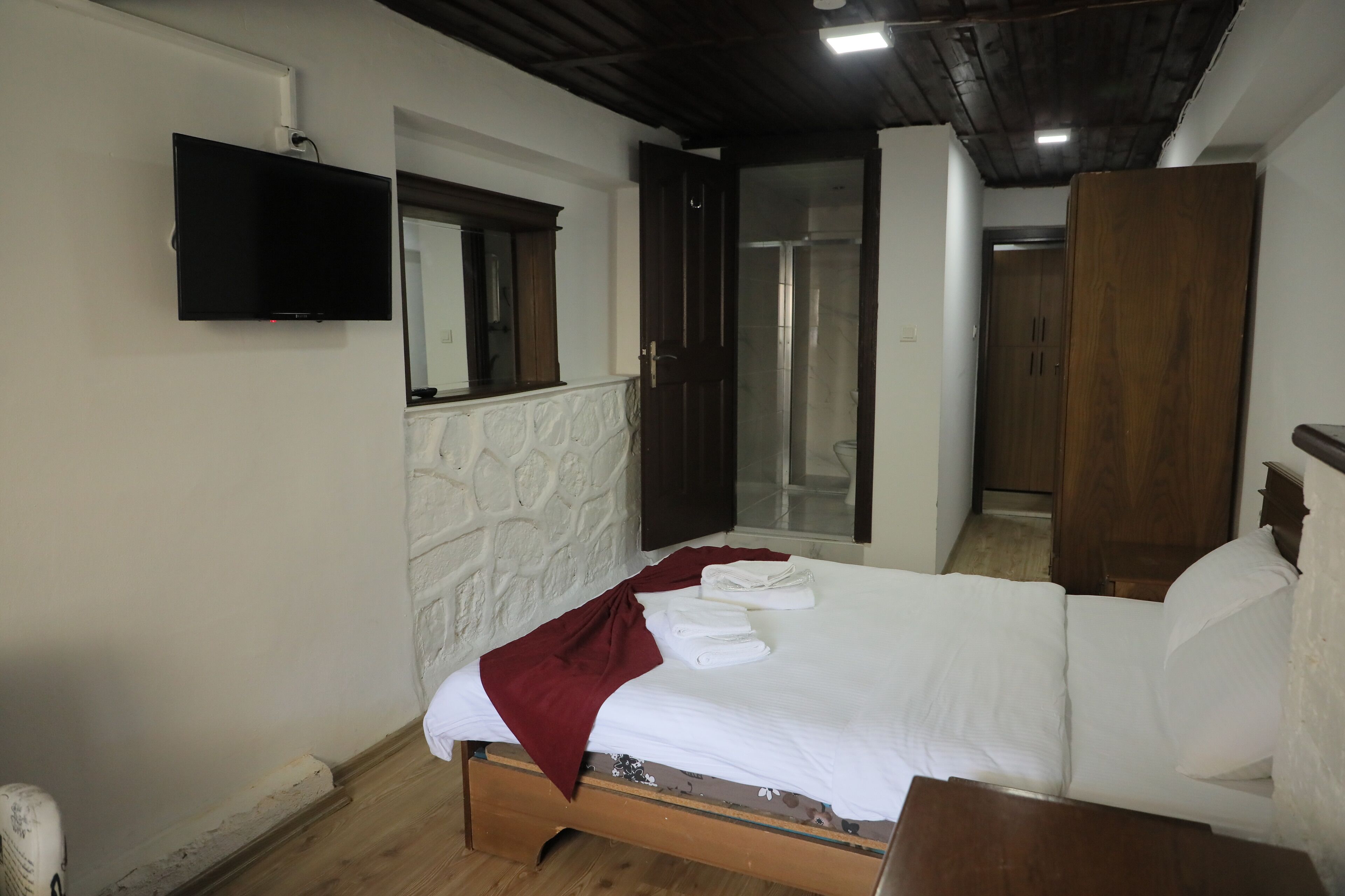 A bedroom with a bed, a flat-screen TV mounted on the wall, and a wooden wardrobe.