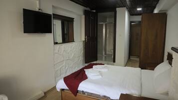 A bedroom with a bed, a flat-screen TV mounted on the wall, and a wooden wardrobe.