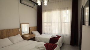 Quarto de hotel com duas camas, cabeceira de madeira, espelho, mesa de cabeceira e janela com cortinas.