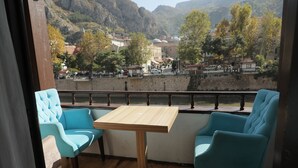 Varanda com duas cadeiras azuis e uma mesa de madeira, com vista para um rio e uma cidade com edifícios e árvores.