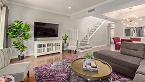 Una sala moderna con televisor de pantalla plana, un mueble blanco, una escalera y un comedor con sillas rojas.