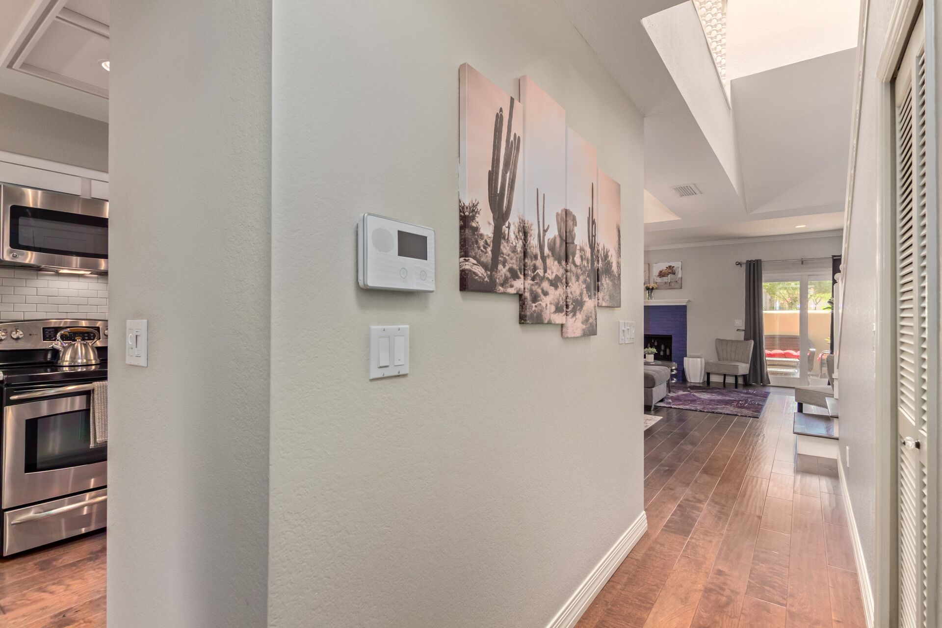 A modern kitchen with stainless steel appliances, a wall-mounted thermostat, and a sliding glass door leading to a living area with a fireplace.