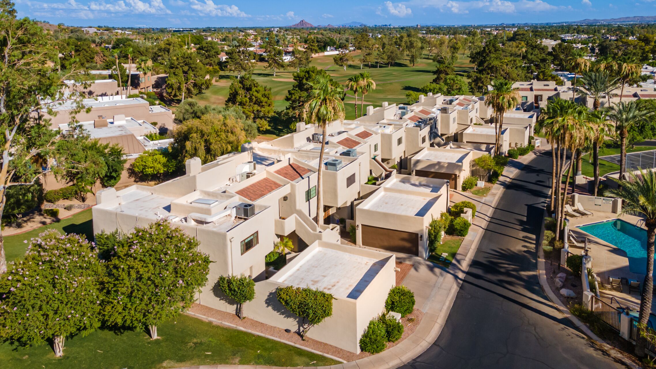 A residential area with modern houses, a swimming pool, and a golf course in the background.