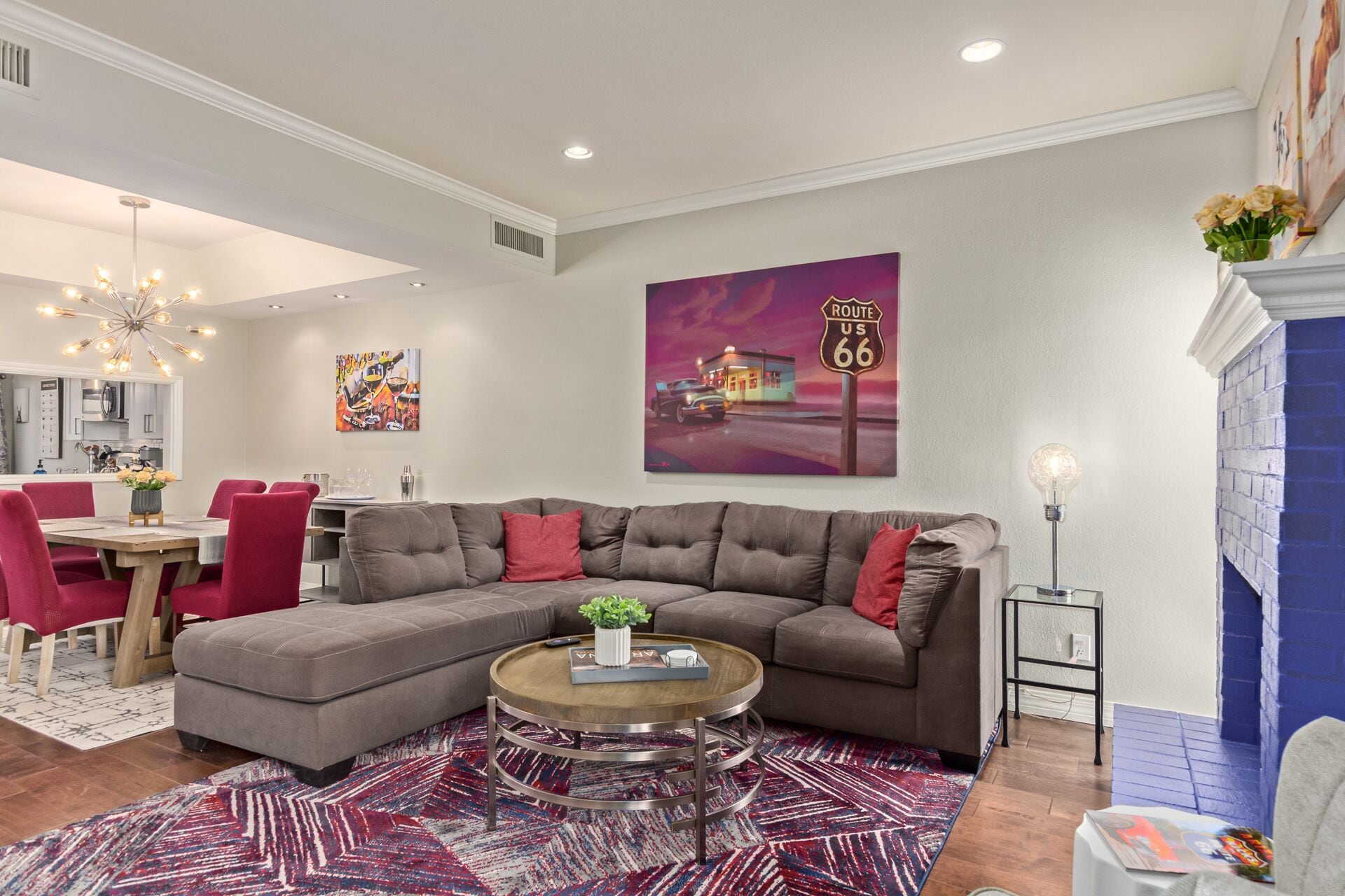 Ein modernes Wohnzimmer mit einem Ecksofa, einem Essbereich mit einem roten Tisch und einer Küche im Hintergrund.