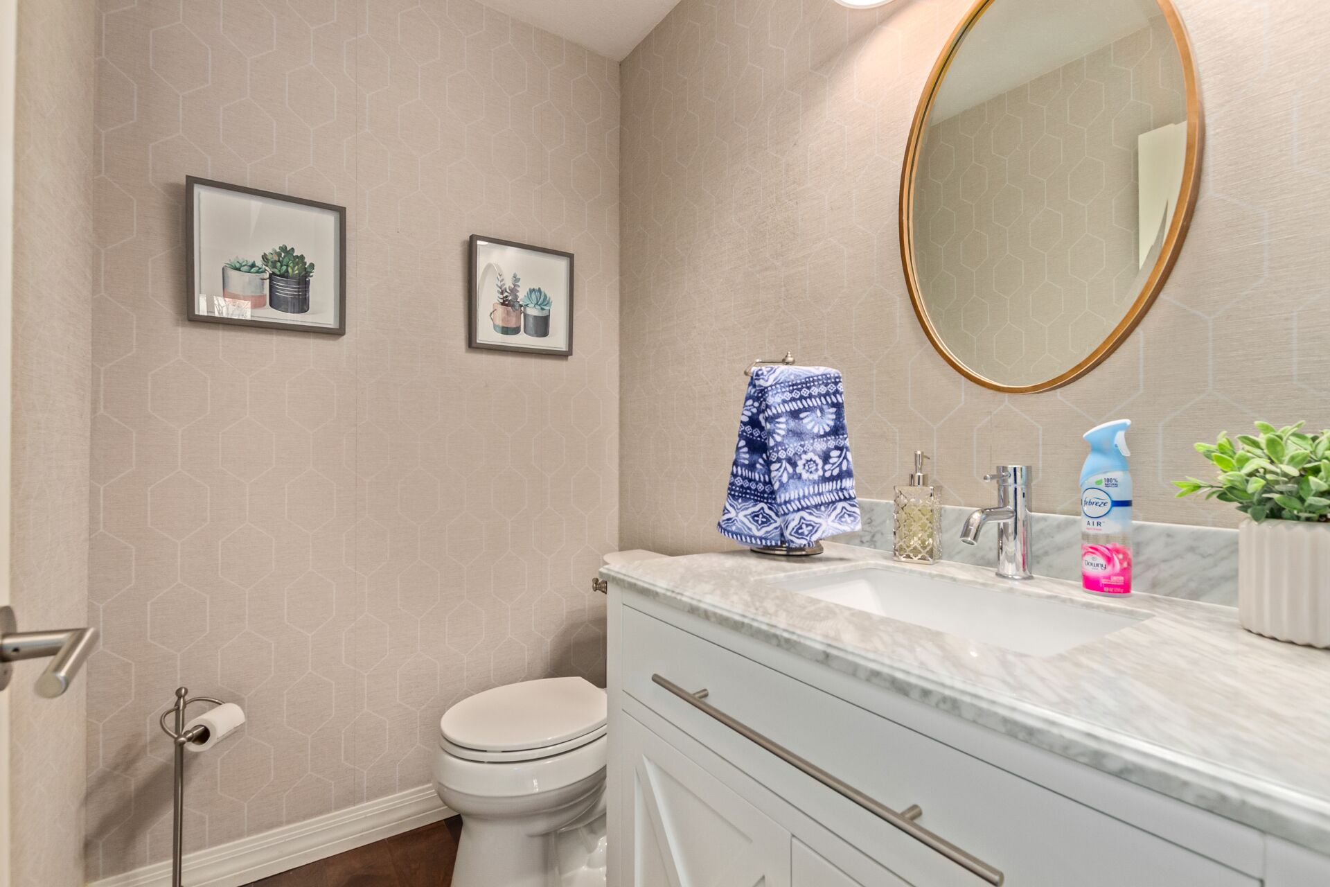 A bathroom with a toilet, a sink with a marble countertop, a mirror, and two framed pictures on the wall.