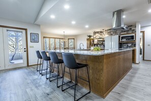A modern kitchen with a large island, bar stools, and a stainless steel range hood.