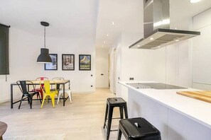 A modern kitchen with white cabinetry, a stainless steel range hood, and a dining area with a table and chairs.