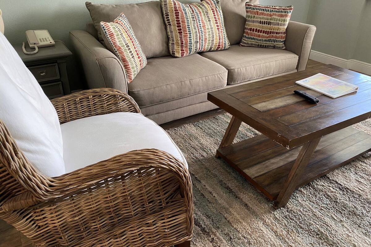 A living room with a beige sofa, two patterned throw pillows, a wicker chair, a wooden coffee table, and a telephone on a side table.