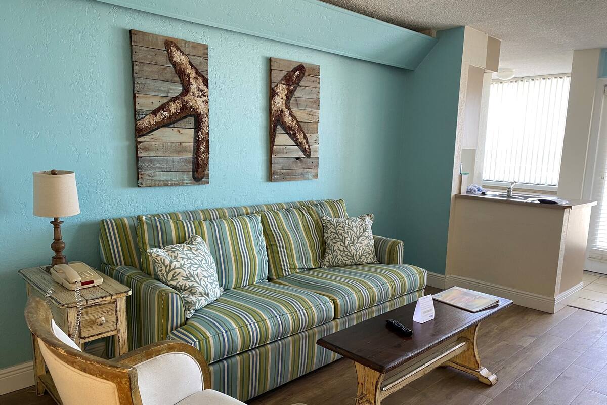 A living room with a striped sofa, a wooden coffee table, a vintage telephone, and two starfish wall art pieces.