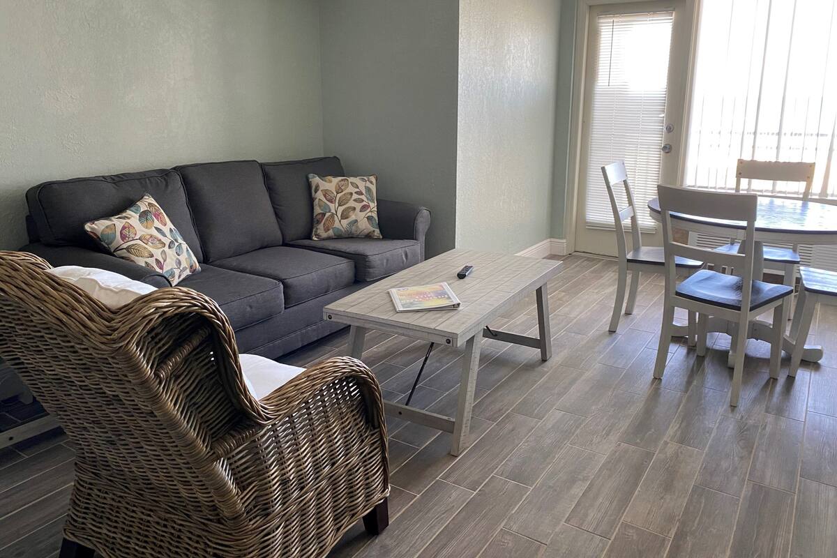 A living room with a grey sofa, wicker chairs, a coffee table, and a dining table with chairs.