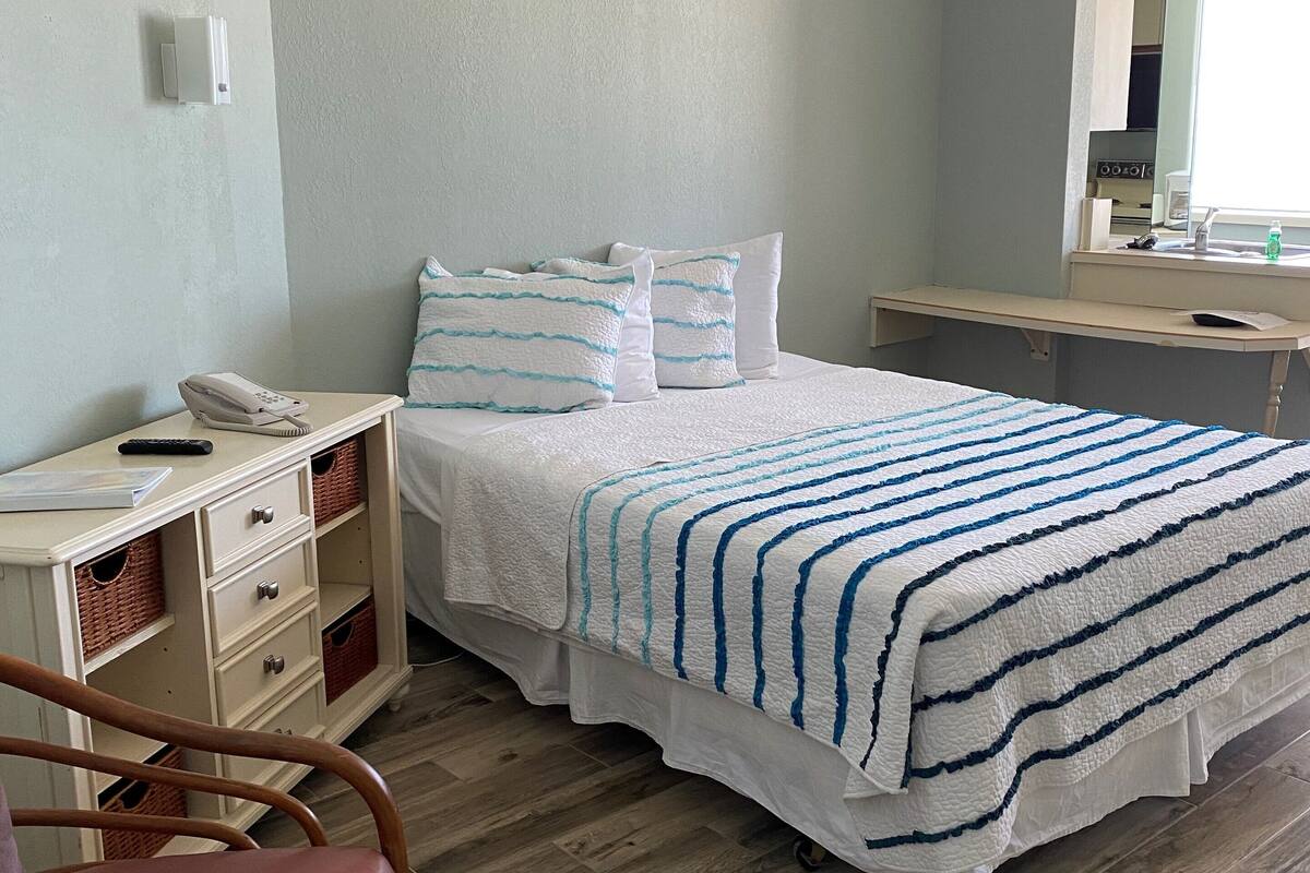 A hotel room with a bed, bedside table, chair, and a mirror.