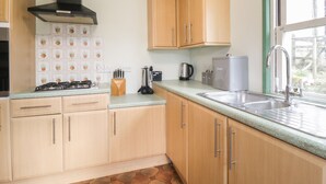 Une cuisine avec des meubles de rangement en bois, une cuisinière à gaz, une bouilloire et un appareil à faire du pain.