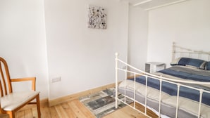 Une chambre avec un plancher en bois, un cadre de lit en métal blanc, une couvre-lit à rayures bleues et grises, une chaise en bois et un petit tapis.