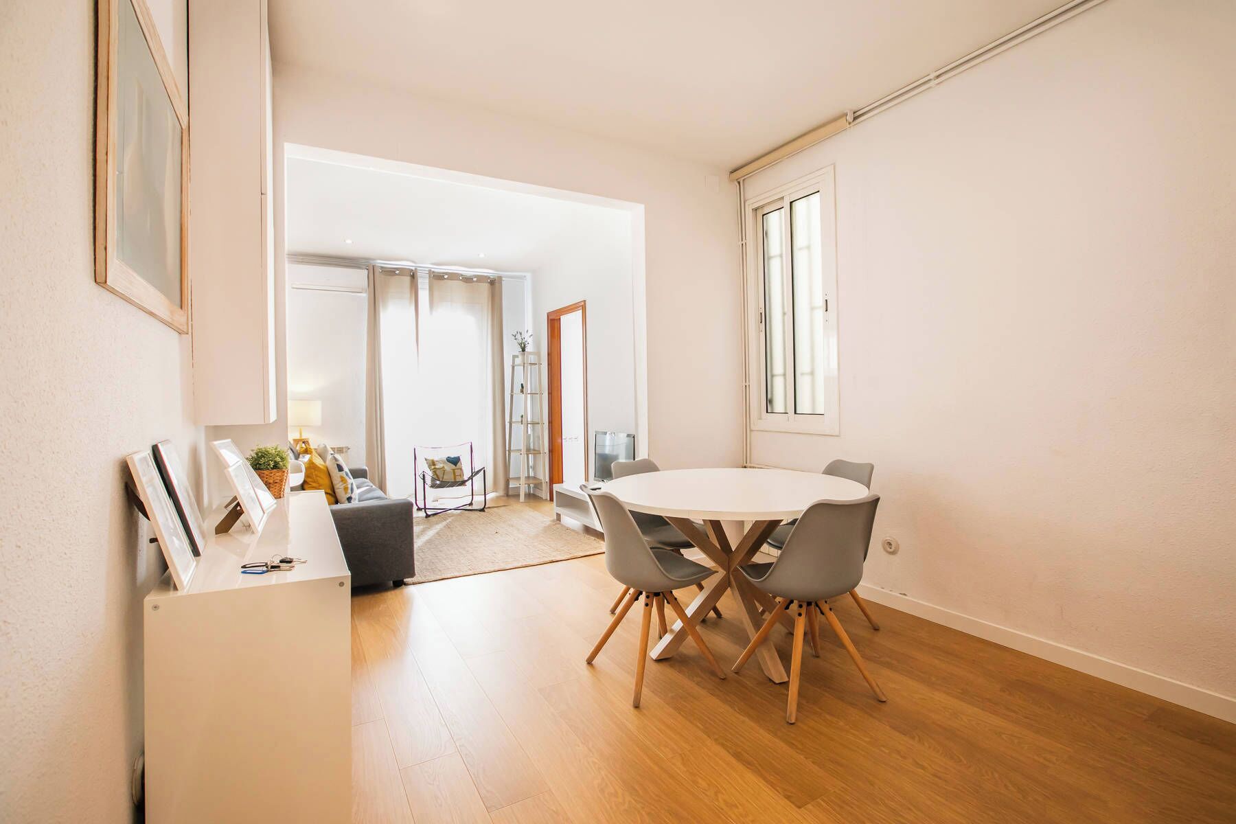 Een moderne woonkamer met een ronde eettafel, grijze stoelen, een grijze bank en een kleine bijzettafel.
