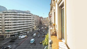 Una calle urbana concurrida con un edificio de varios pisos, balcones y una pasarela para peatones.