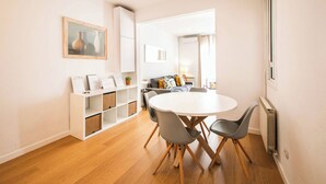 Un salón moderno con una mesa redonda de comedor, sillas grises, un sofá gris con cojines amarillos, un armario blanco y un cuadro en la pared.