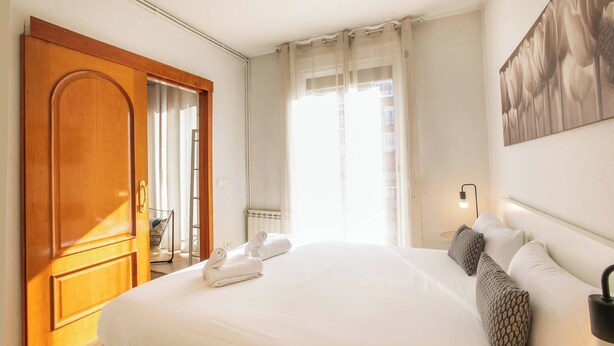 Habitación de hotel con una cama grande, un armario de madera, una ventana con cortinas traslúcidas y una obra de arte colgada en la pared.