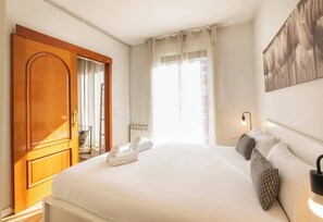 Une chambre d’hôtel avec un grand lit, une armoire en bois, une fenêtre avec des rideaux légers et une œuvre d’art accrochée au mur.
