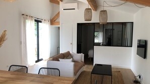 Un soggiorno moderno con un tavolo da pranzo in legno, un divano e un tavolino da caffè nero. Si nota un'ampia finestra con tende, una ventola a soffitto e un televisore a parete.