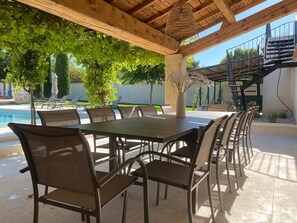 A covered outdoor dining area with a pool in the background.