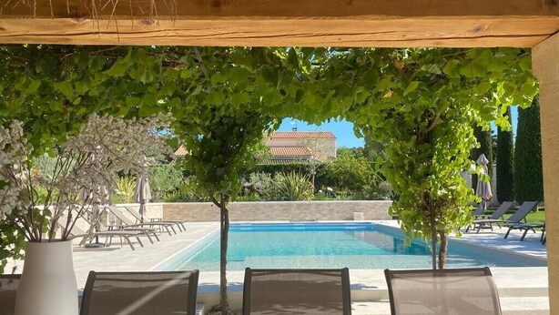 Area piscina con un gazebo in legno, poltrone relax e vista su un edificio sullo sfondo.