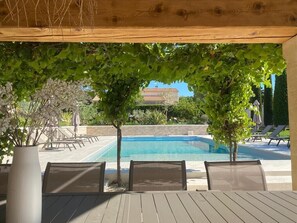 A poolside area with a wooden pergola, lounge chairs, and a view of a building in the background.