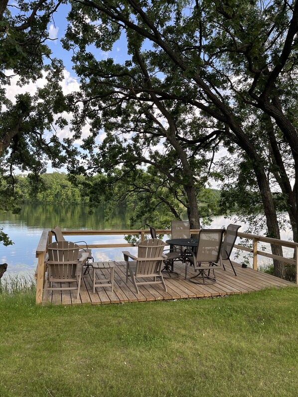 A wooden deck with chairs and a table overlooking a calm lake, surrounded by trees.