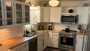 Una cocina con armarios blancos, microondas, estufa y cafetera.