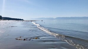 A beach with calm waters, a clear sky, and distant mountains. - Points West Oceanfront Resort 3 bedroom Ocean Point Beach House  (Sooke)